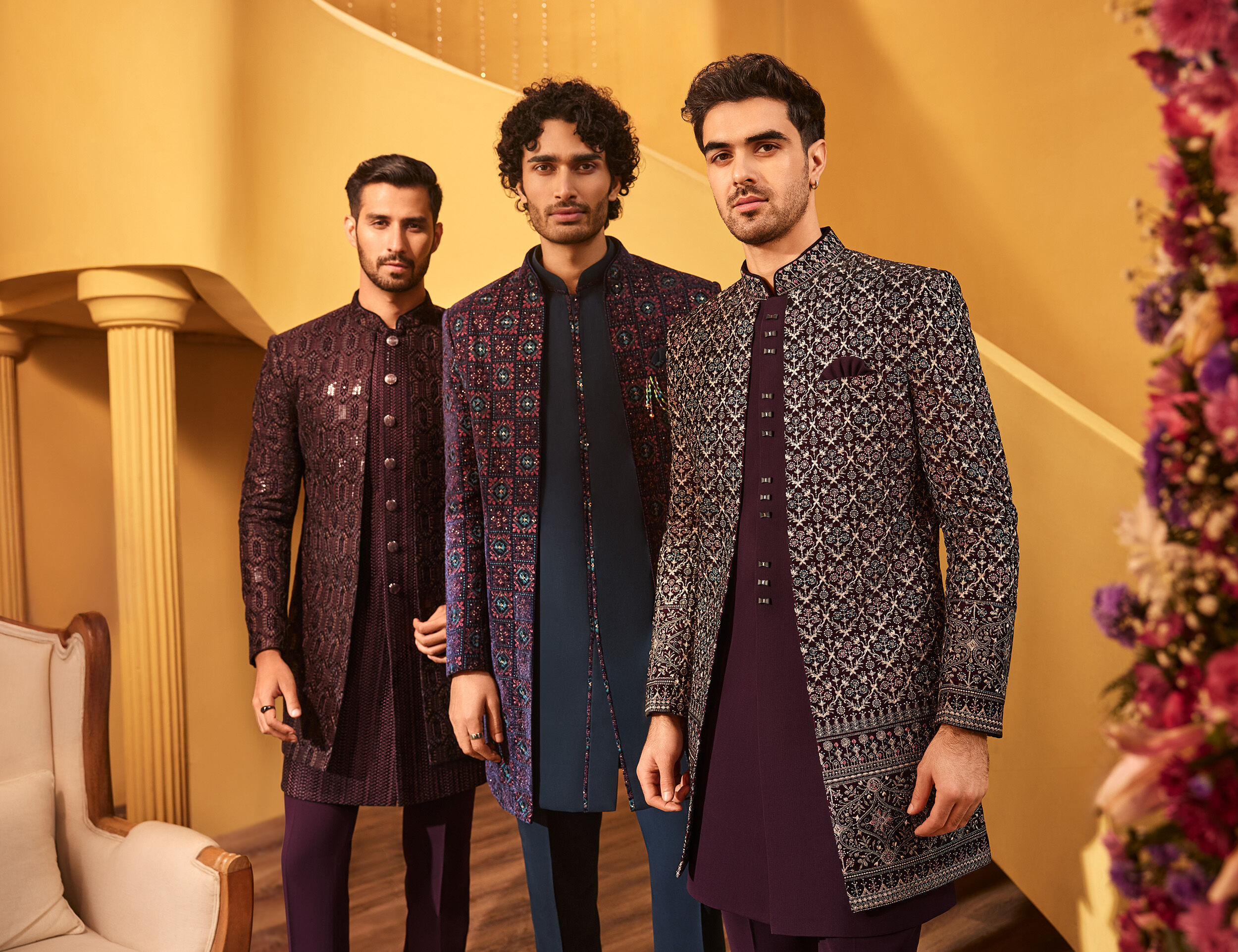 Three men in intricately embroidered designer sherwanis posing in a luxurious wedding setting
